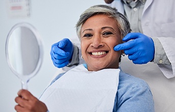 Woman smiling while holding mirror with dentist